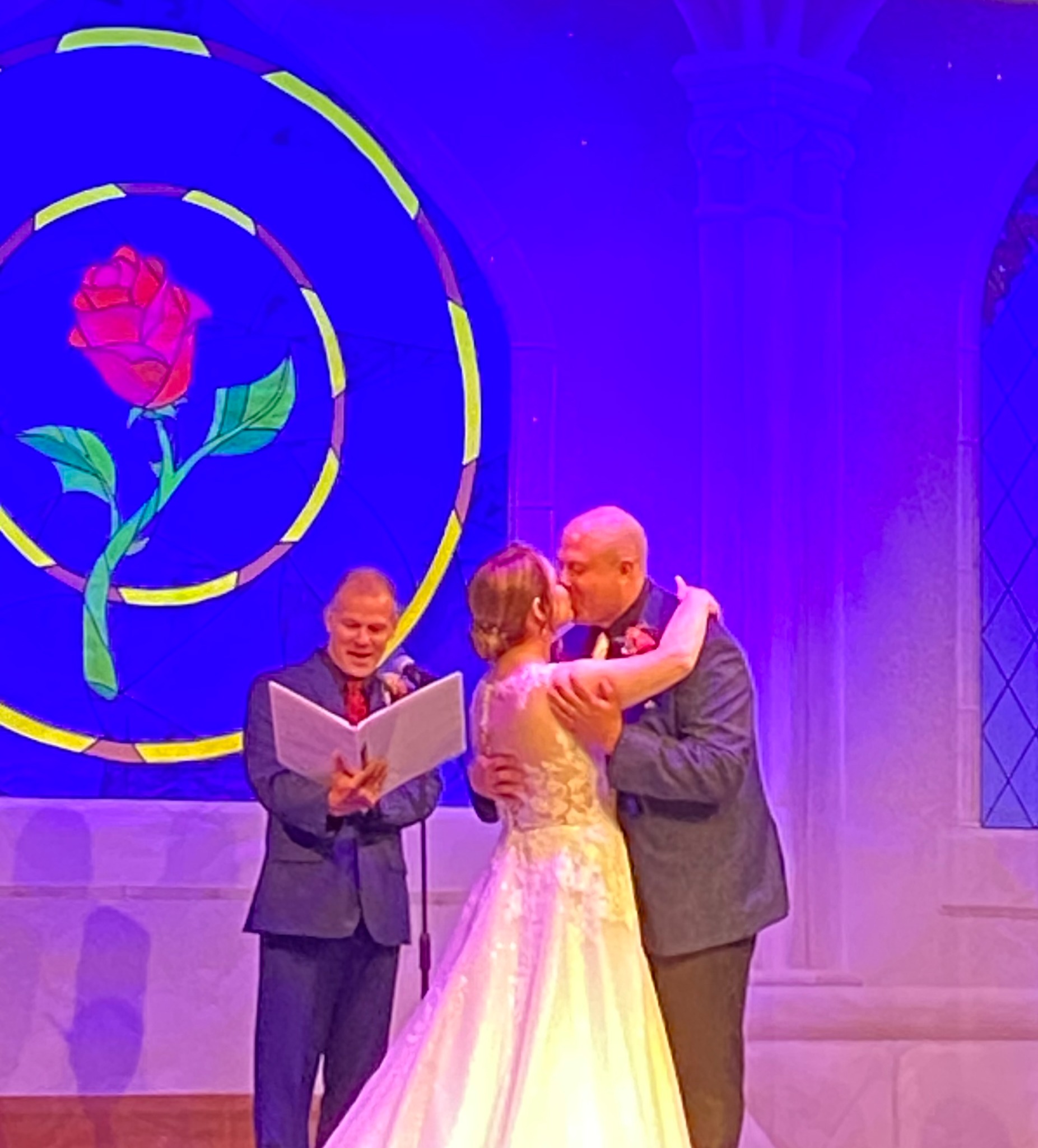 A couple sharing a kiss during their wedding ceremony, with their officiant alongside them.